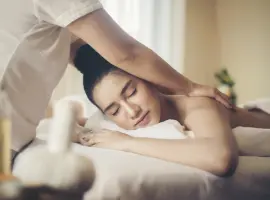 A woman receiving a shoulder massage while lying on a spa bed, looking relaxed and content.